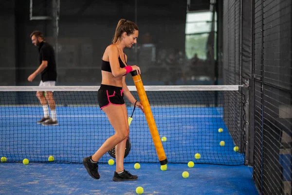 Kız kortun ortasında raket ya da tenis topu topluyor.