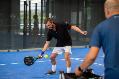 Öğrencisi Padel 'in erkek öğrencisine ders verirken gözlemci çocuğa kapalı tenis kortunda nasıl Padel oynanacağını öğretiyor.
