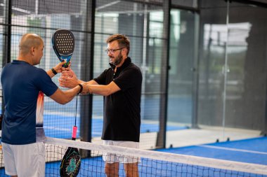 Öğrencisi Padel 'in erkek öğrencisine ders verirken gözlemci çocuğa kapalı tenis kortunda nasıl Padel oynanacağını öğretiyor.