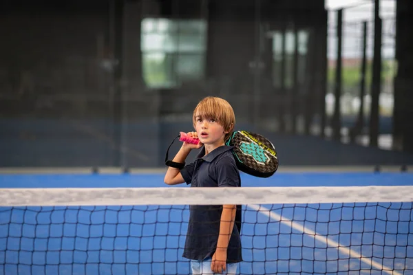 Öğrencisi Padel 'den çocuğa ders verirken gözlemci, küçük çocuğa kapalı tenis kortunda nasıl padel oynanacağını öğretiyor.