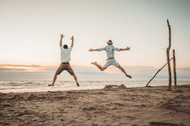 Mutlu arkadaşlar yaz tatillerini gün batımında kumsalda geçiriyorlar - iki çocuk güneşin doğuşunda plajda zıplıyor - tatil kavramı