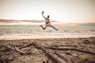Mutlu çocuk yaz tatillerini gün batımında sahilde geçiriyor genç adam güneşin doğuşunda plajda zıplıyor.