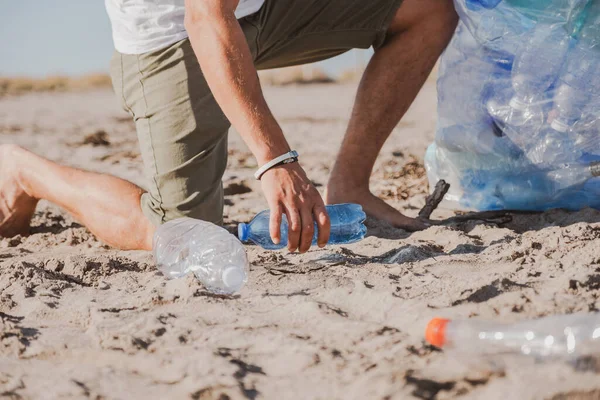 Genç adam plastik şişe topluyor ve plaj gönüllüsü konseptini temizliyor. Plastiksiz. B gezegenimiz yok. Dünyayı plastikten kurtar