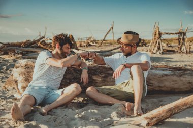 İki çocuk sahilde oturup birbirlerini yumruklarıyla selamlıyorlar. Gençler birbirini selamlamak için yumruklarını sallıyor.