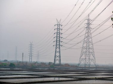 Deniz tuzu tarlasında ve güneş batarken ahırda yüksek voltajlı elektrik hatlarının yansıması.