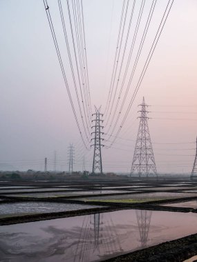 Deniz tuzu tarlasında ve güneş batarken ahırda yüksek voltajlı elektrik hatlarının yansıması.