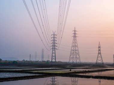 Deniz tuzu tarlasında ve güneş batarken ahırda yüksek voltajlı elektrik hatlarının yansıması.