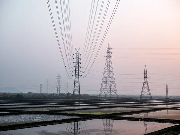 Deniz tuzu tarlasında ve güneş batarken ahırda yüksek voltajlı elektrik hatlarının yansıması.
