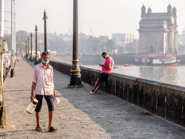 Mumbai, Hindistan - 7 Ocak 2021: COVID 19 veya koronavirüs salgınıyla ilgili bir maske takan ve Mumbai 'de ünlü bir turistik yer olan Hindistan Kapısı yakınında çay satan kimliği belirsiz bir adam