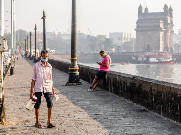 Mumbai, Hindistan - 7 Ocak 2021: COVID 19 veya koronavirüs salgınıyla ilgili bir maske takan ve Mumbai 'de ünlü bir turistik yer olan Hindistan Kapısı yakınında çay satan kimliği belirsiz bir adam