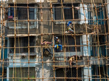 Mumbai, Hindistan - 20 Mart 2021: İnşaat işçileri bina bakımını başlatmak için bir duvara bambu yapı inşa ediyorlar. Koruyucu vites yok..