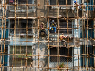 Mumbai, Hindistan - 20 Mart 2021: İnşaat işçileri bina bakımını başlatmak için bir duvara bambu yapı inşa ediyorlar. Koruyucu vites yok..