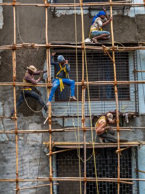 Mumbai, Hindistan - 20 Mart 2021: İnşaat işçileri bina bakımını başlatmak için bir duvara bambu yapı inşa ediyorlar. Koruyucu vites yok..