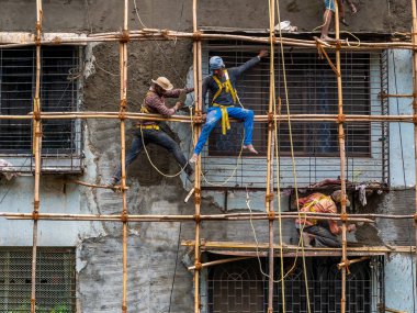 Mumbai, Hindistan - 20 Mart 2021: İnşaat işçileri bina bakımını başlatmak için bir duvara bambu yapı inşa ediyorlar. Koruyucu vites yok..