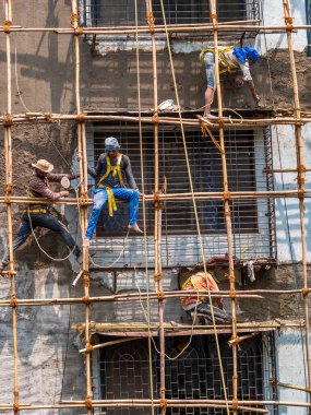 Mumbai, Hindistan - 20 Mart 2021: İnşaat işçileri bina bakımını başlatmak için bir duvara bambu yapı inşa ediyorlar. Koruyucu vites yok..