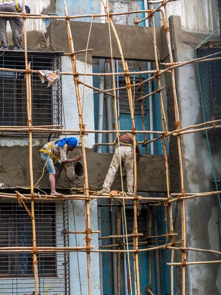 Mumbai, Hindistan - 20 Mart 2021: İnşaat işçileri bina bakımını başlatmak için bir duvara bambu yapı inşa ediyorlar. Koruyucu vites yok..