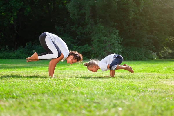 年轻的女人和小女孩一起在一个绿色的公园里练习瑜伽 并展示了起重机的姿势或面包圈 — 图库照片