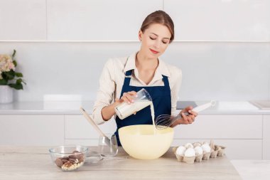 Mavi önlüklü kadın pastacı büyük kaseye süt döküyor. Turta ya da kek yapma süreci