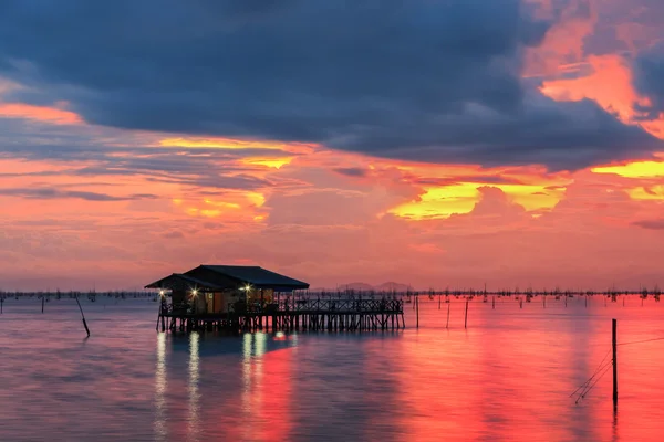 Nubes oscuras sobre el lago con cielo rojo y cabaña de madera en la superficie al atardecer — Foto de Stock