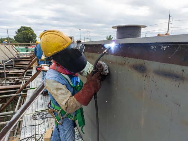 Kaynakçı, Flux Cored Arc Welding (FCAW) işlemiyle bir çelik yapı çalışması yapıyor ve endüstriyel fabrikada güvenlik için kişisel koruyucu ekipman (PPE) ile uygun şekilde giyiniyor.