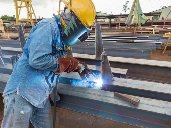 The welder is welding a steel structure work with process Flux Cored Arc Welding(FCAW) and dressed properly with personal protective equipment(PPE) for safety, at industrial factory.