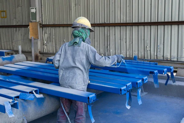 Painter is working to painting color top coat on steel structure with spray gun, at industrial factory.