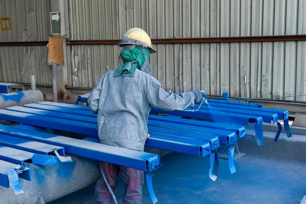 Painter is working to painting color top coat on steel structure with spray gun, at industrial factory.