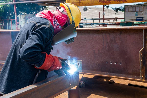 Welder is welding a steel plate for steel structure work with process Flux Cored Arc Welding(FCAW) and dressed properly with personal protective equipment(PPE) for safety, at industrial factory.