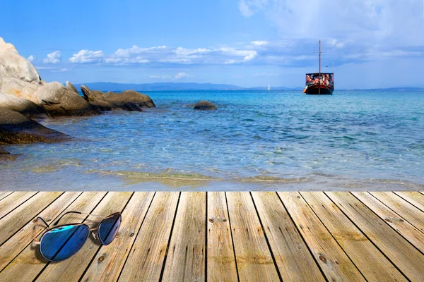 Cais de madeira com óculos de sol, ao lado da praia tropical da Grécia — Fotografia de Stock