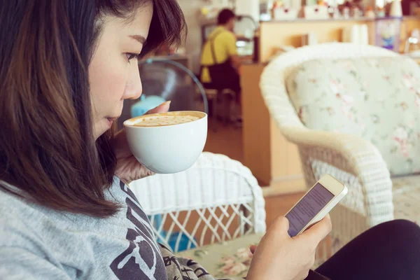 女性の飲酒はカフェでコーヒーをホットし、携帯電話を使用 — ストック写真