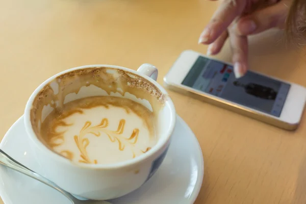 Caramelo macchiato café e mão mulher usando um telefone móvel — Fotografia de Stock