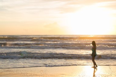 Sahilde, sabah yaz gün ışığında yürüyen kadın