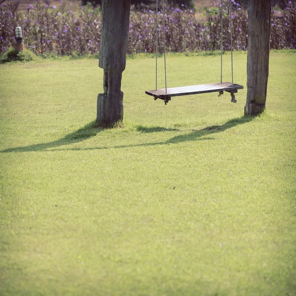Playground swing made wood hanging in green grass field — Stock Photo, Image
