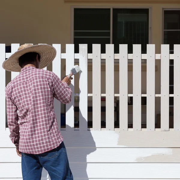 Dělník, natřené bílým plotem s kartáčem — Stock fotografie