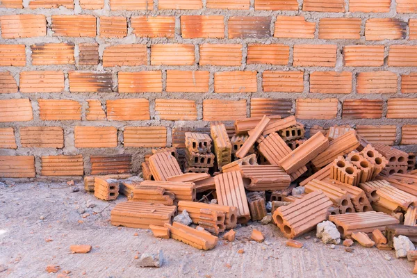 Pile of bricks in construction site with brick wall background — Stock Photo, Image