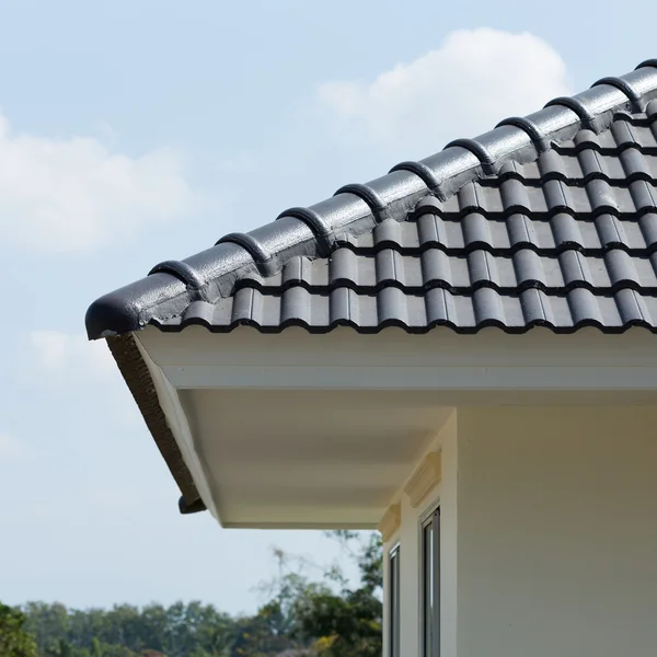 Zwarte dakpannen op huis met blauwe hemel — Stockfoto