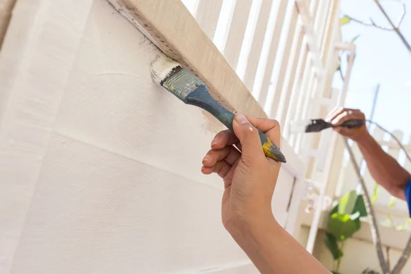 Mão trabalhador segurando pintura escova branco na cerca de madeira — Fotografia de Stock