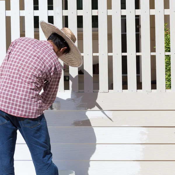Dělník, natřené bílým plotem s kartáčem — Stock fotografie
