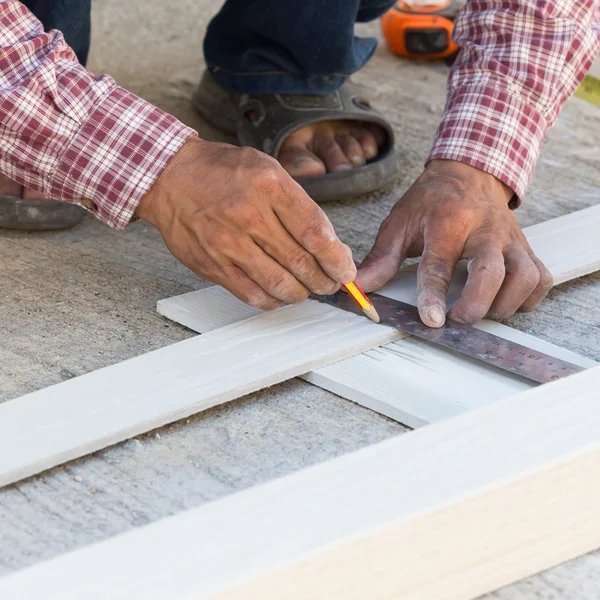 Carpintero usando regla para dibujar una marca de línea en un tablero de madera — Foto de Stock