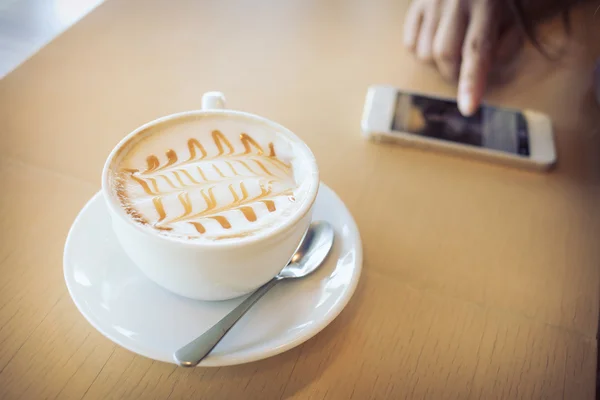 木製のテーブルでの携帯電話のバーで熱いコーヒーを飲むの — ストック写真