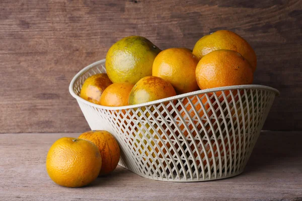 Oranžové ovoce v bílých koše na dřevo stůl pozadí — Stock fotografie