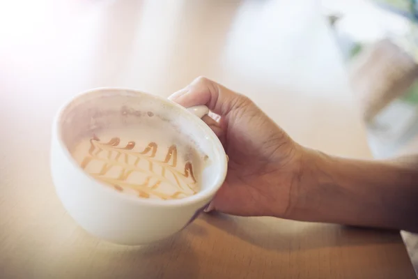 Mulher mão segurando xícara de café caramelo macchiato quente de café — Fotografia de Stock