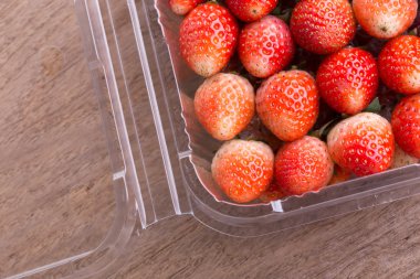 plastik kutu ambalaj ahşap masa üzerinde kırmızı olgun çilek