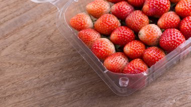 plastik kutu ambalaj ahşap masa üzerinde kırmızı olgun çilek