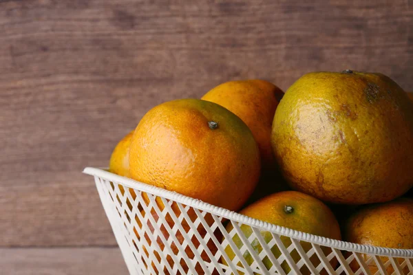 Ahşap masa arka plan üzerinde beyaz sepet içinde turuncu meyve — Stok fotoğraf