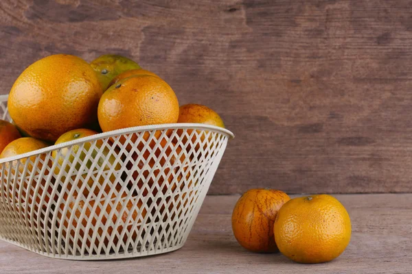 Oranžové ovoce v bílých koše na dřevo stůl pozadí — Stock fotografie