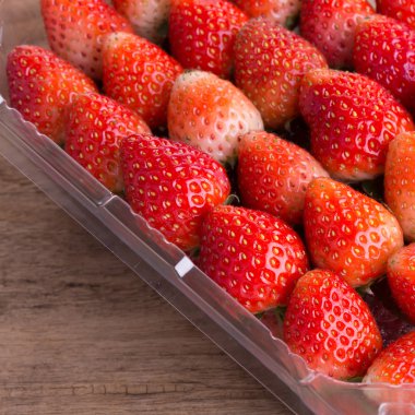 plastik kutu ambalaj ahşap masa üzerinde kırmızı olgun çilek