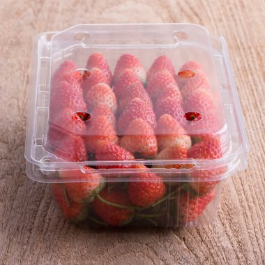 plastik kutu ambalaj ahşap masa üzerinde kırmızı olgun çilek