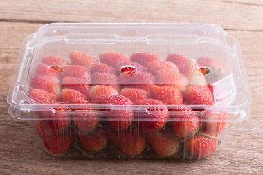 plastik kutu ambalaj ahşap masa üzerinde kırmızı olgun çilek