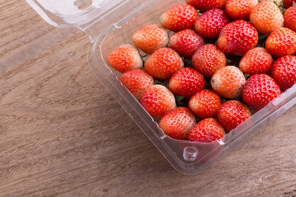 plastik kutu ambalaj ahşap masa üzerinde kırmızı olgun çilek